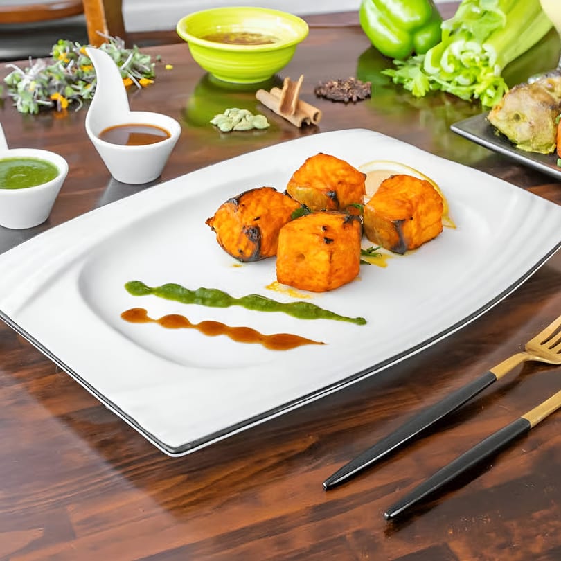 Indian paneer tikka with green and brown sauces, spices, and vegetables on a wooden table.