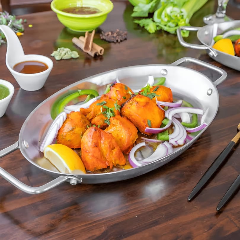 Indian chicken tikka with onions, peppers, and lemon in a metal serving dish.