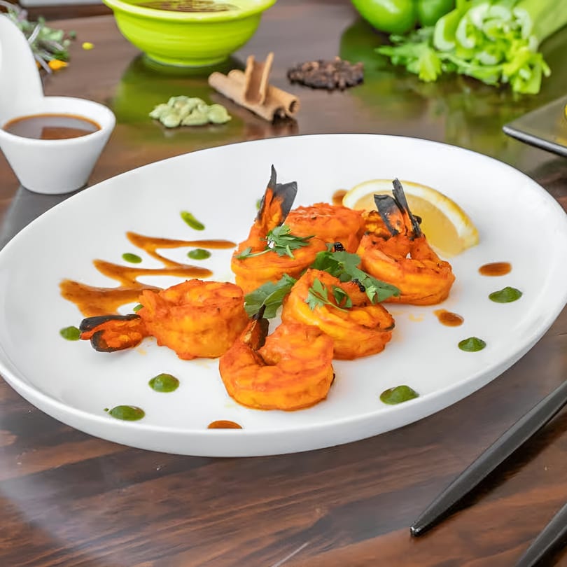 Indian tandoori shrimp with lemon, cilantro, and sauces on a white plate.